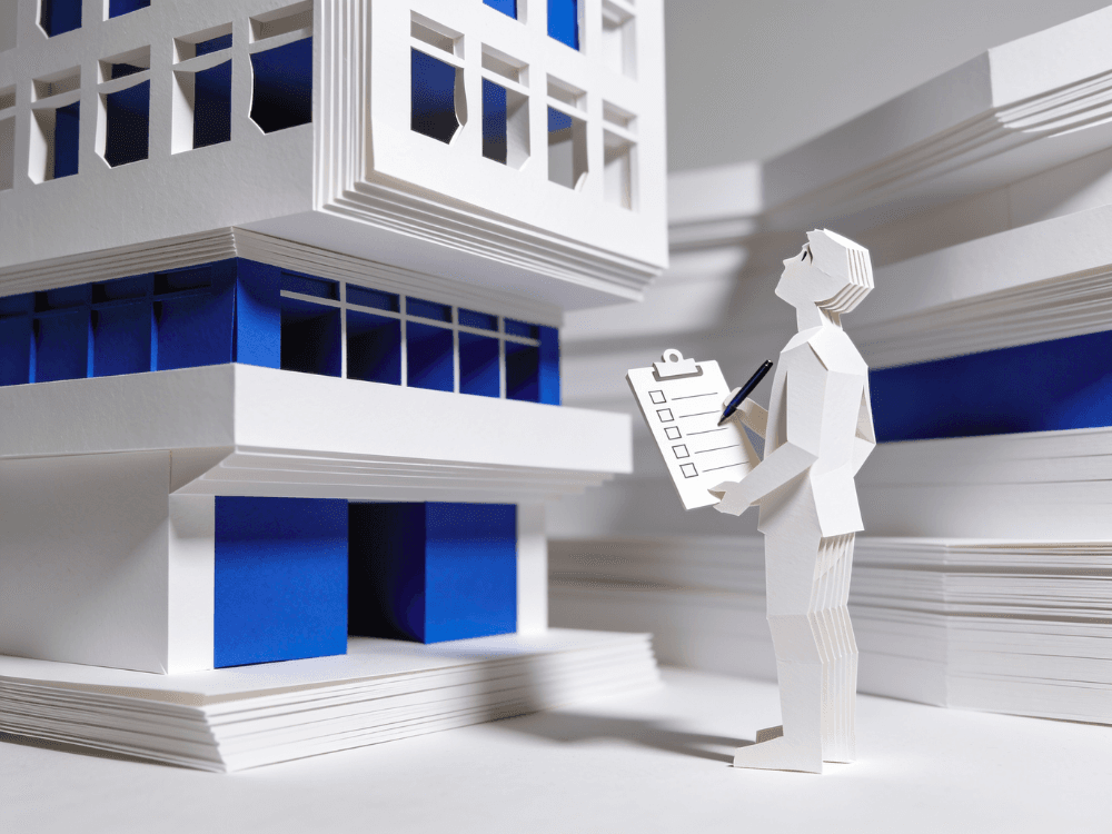 Papercraft figure with a checklist inspecting a multi-storey building