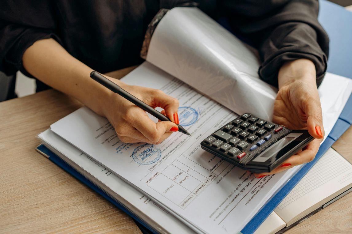 Hands reviewing financial documents with a calculator, representing institutional governance, compliance, and regulatory oversight in investment processes