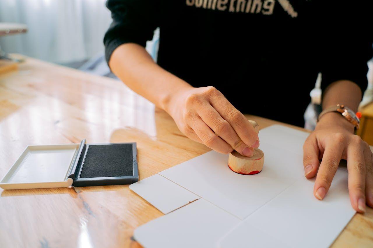 Hands stamping official documents on a desk, representing SEC-aligned regulatory compliance, verification, and legally validated investment processes